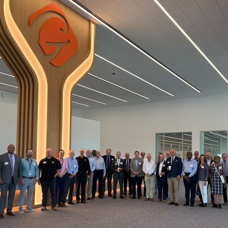 Group of professionals at a corporate event in a modern office space featuring a large logo, symbolizing unity and collaboration.