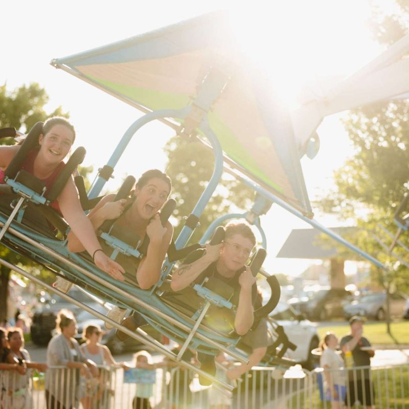 People enjoying a thrill ride at a sunny amusement park, showcasing excitement and fun outdoors.
