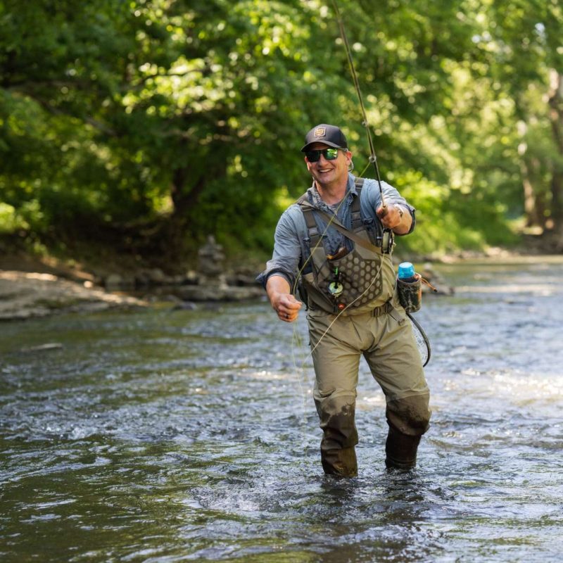 Angler joyfully fly fishing in a sunny river, capturing the essence of outdoor adventure.