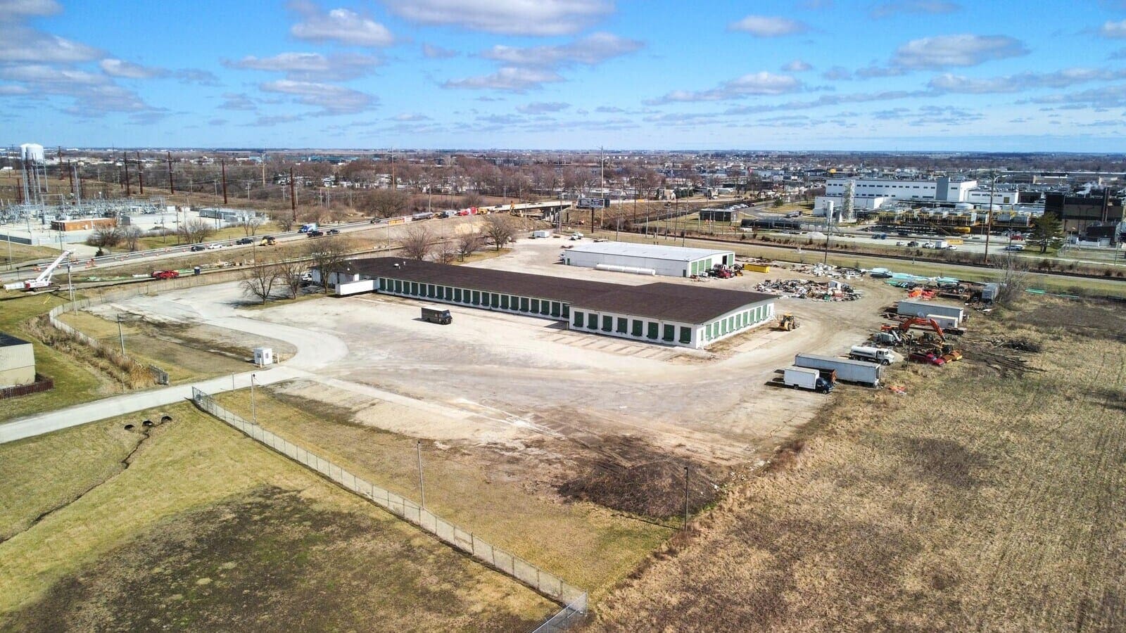 Storage facility with multiple units on a spacious lot, located near an industrial area under a clear blue sky.