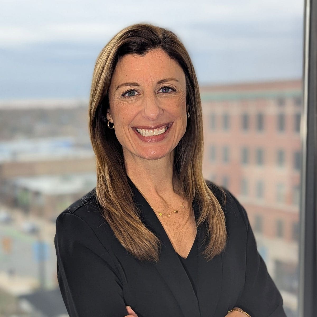 Smiling professional in a black blazer by office window, representing company leadership.