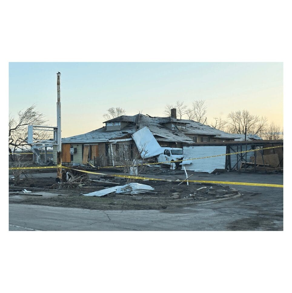 Damaged house with roof debris and caution tape, likely after a severe storm.