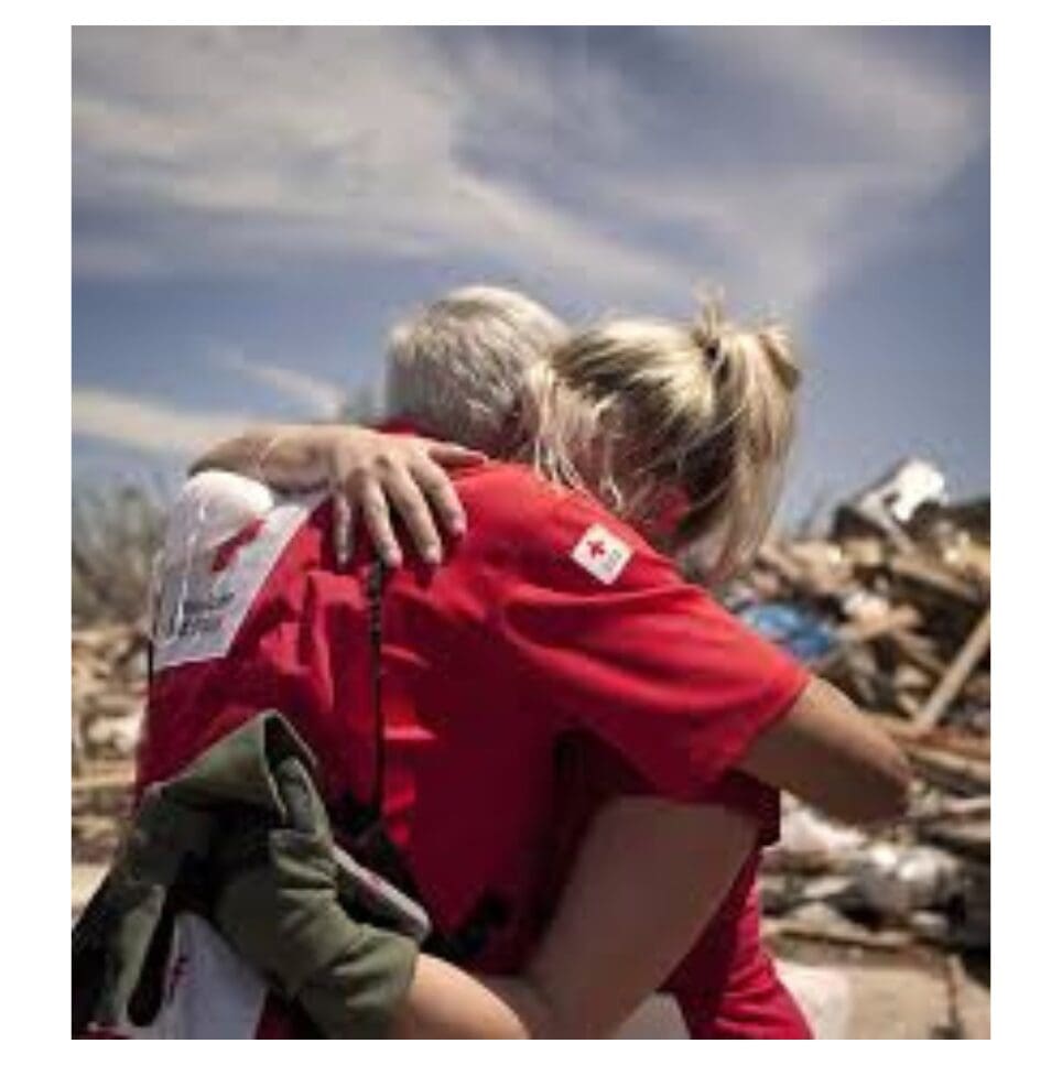 Two Red Cross volunteers embrace amid disaster debris.